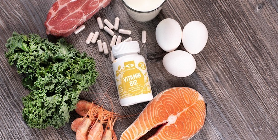 B12 capsules placed on a wooden board with a piece of meat, a piece of salmon, shrimp, eggs and milk